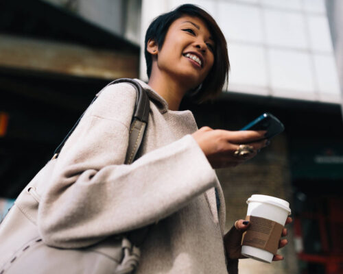 woman walking in an urban setting with phone and coffee